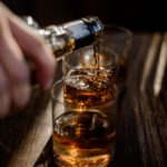 Pouring strong alcohol drink into the glasses which are on the wooden table