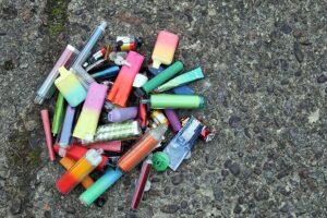 A collection of discarded electronic cigarette vapes have been collected and placed together over a worn concrete floor